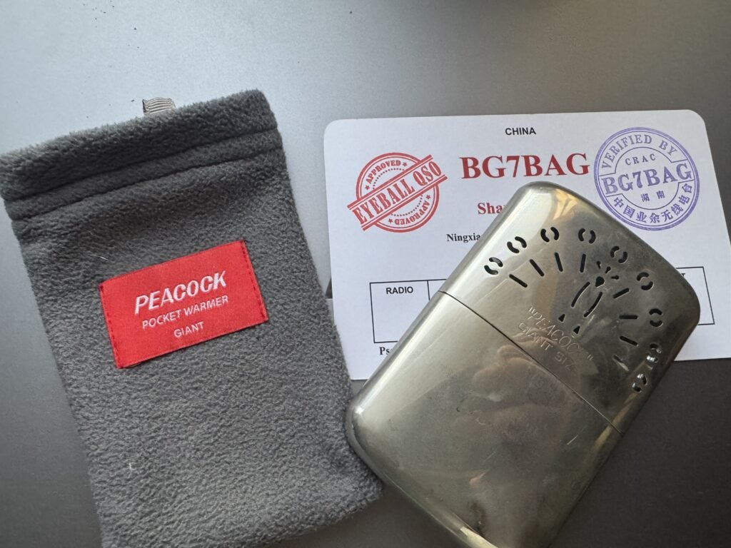 PEACOCK Giant catalytic pocket warmer with grey flannel pouch, photographed on a BG7BAG QSL card